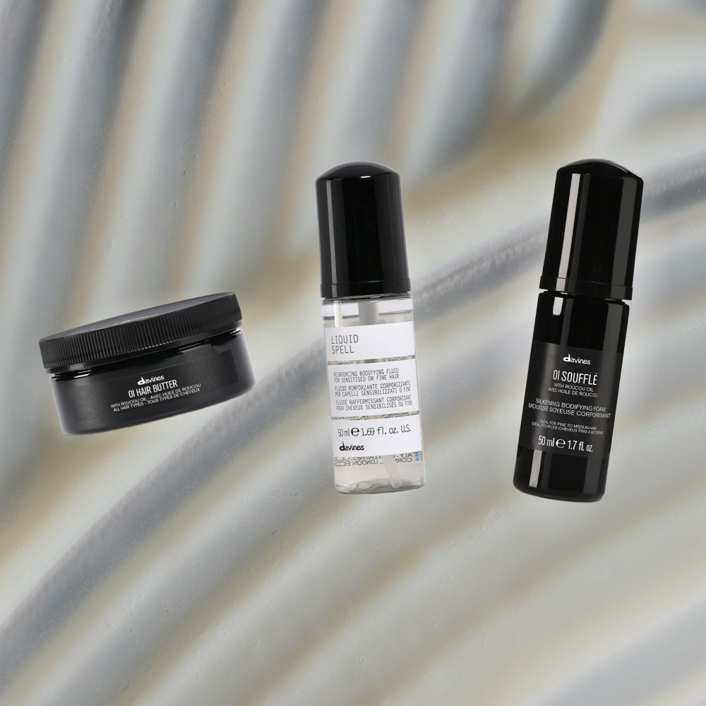Davines Mini OI Hair Butter, Mini Liquid Spell Reinforcing Bodifying Fluid, and Mini OI Soufflé on textured grey background